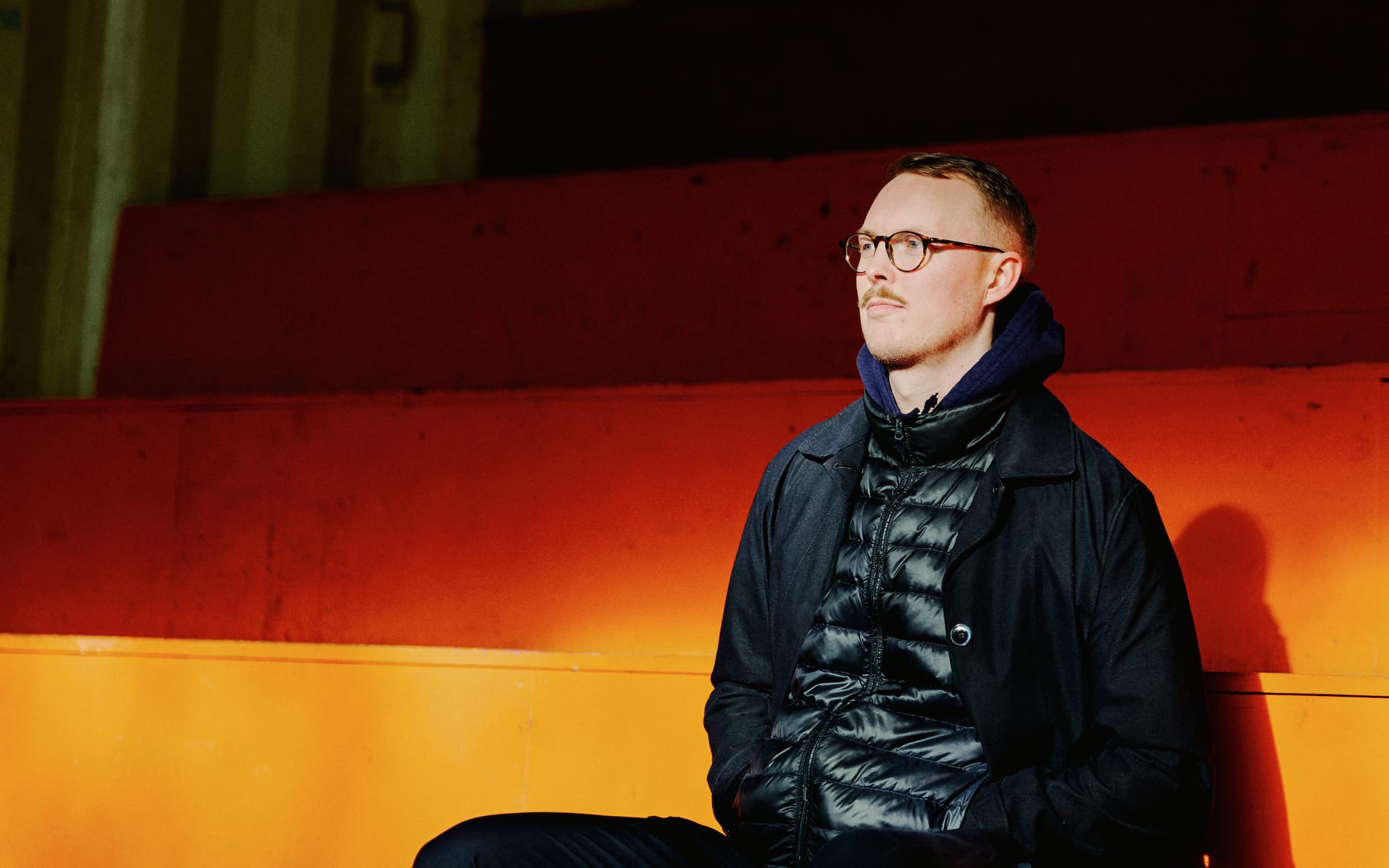 Christian Højbo Møller sidder på en orange betontrappe i skarpt lys og kigger ud til siden